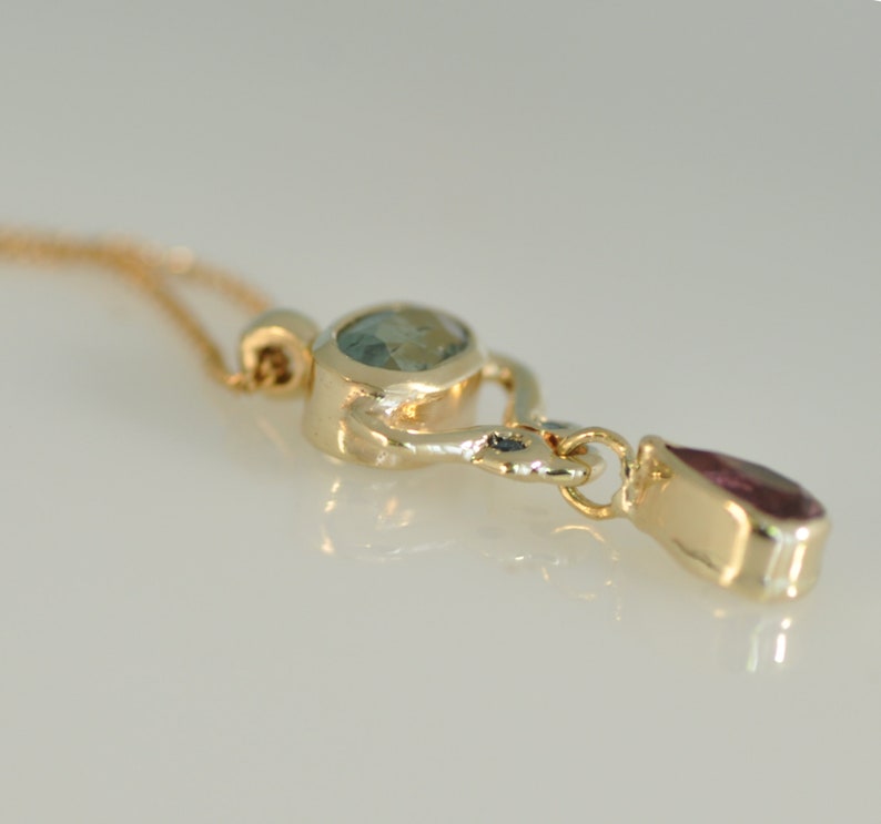 May include: A gold pendant necklace with a light blue oval gemstone and a teardrop-shaped pink gemstone.