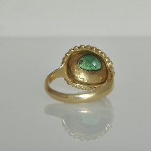 May include: A gold ring with a green gemstone set in a bezel setting. The ring is decorated with a beaded edge.