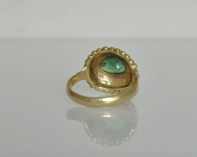May include: A gold ring with a green gemstone set in a bezel setting. The ring is decorated with a beaded edge.
