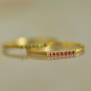 May include: A gold ring with a row of small pink gemstones. The ring is simple and delicate.