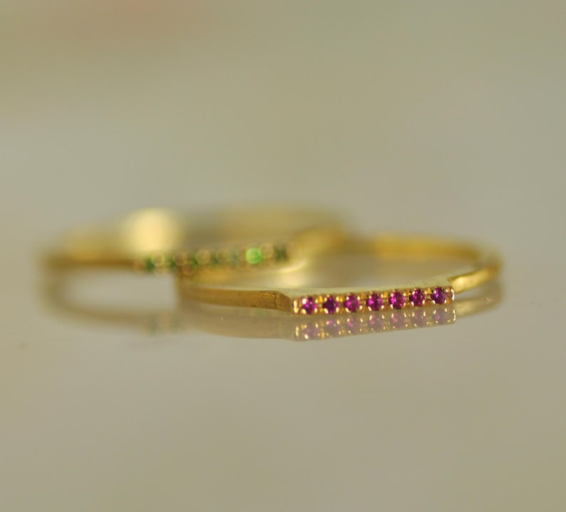 May include: A gold ring with a row of small pink gemstones. The ring is simple and delicate.