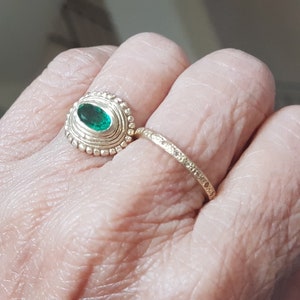 May include: A gold ring with a green oval gemstone set in a beaded bezel. A second, thinner gold band is worn on the same finger.