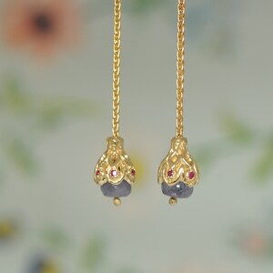 May include: A pair of gold dangle earrings with a delicate chain and a purple gemstone accented with small red gemstones.