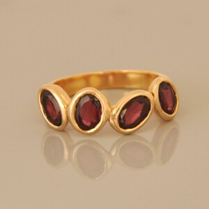 Puede incluir: Un anillo de oro con cuatro piedras ovaladas de color rojo oscuro engastadas en la banda.
