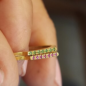 May include: Two gold rings with a row of small green and pink gemstones. The rings are stacked on top of each other.