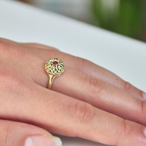 May include: A gold ring with a red gemstone surrounded by green gemstones.
