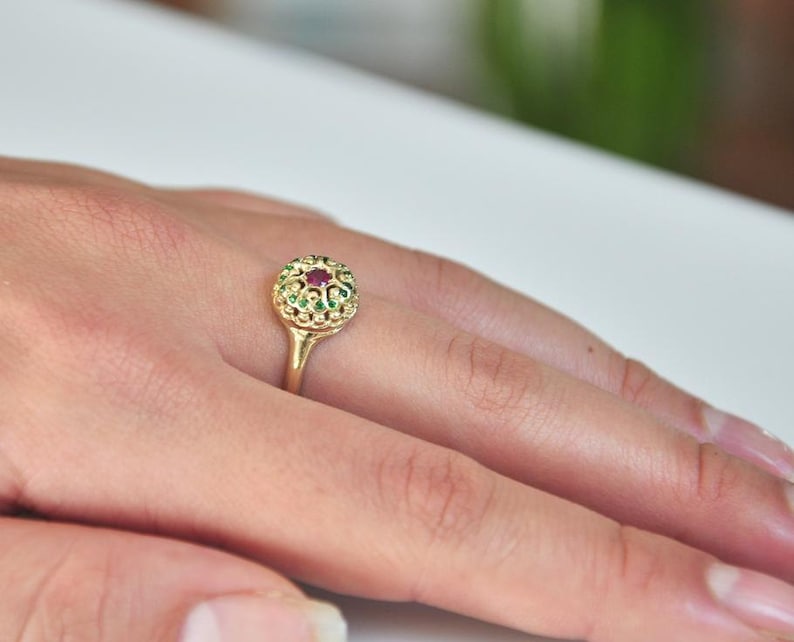 May include: A gold ring with a red gemstone surrounded by green gemstones.