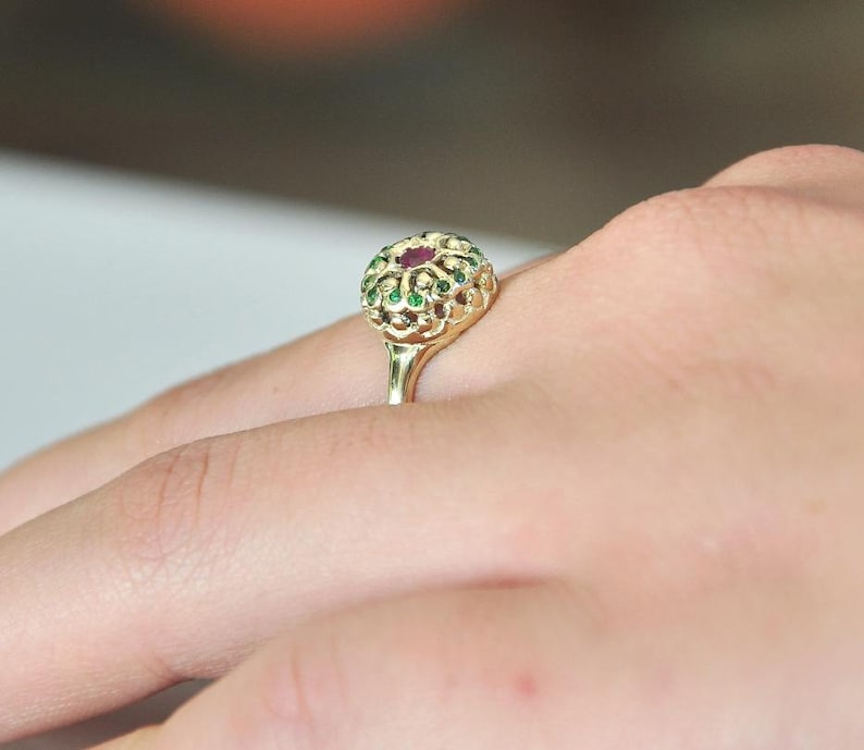 May include: A gold ring with a red and green gemstone setting. The ring is on a person's finger.