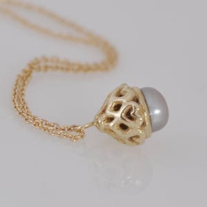 May include: A gold chain necklace with a delicate pendant featuring a pearl set in a gold filigree design.