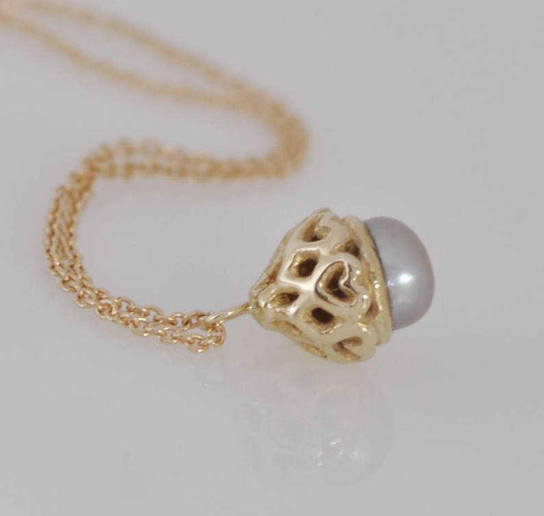 May include: A gold chain necklace with a delicate pendant featuring a pearl set in a gold filigree design.