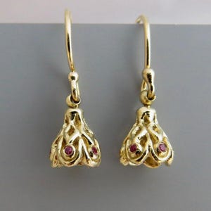 Peut inclure: Une paire de boucles d'oreilles pendantes en or avec un motif en filigrane ajouré en forme de cloche. Chaque boucle est ornée de petites pierres précieuses rondes rose foncé incrustées dans le treillis métallique et suspendue à un crochet.