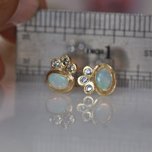Op de afbeelding: Een paar gouden oorbellen met ovale opalen en kleine blauwe edelstenen. De oorbellen zijn geplaatst tegen een witte achtergrond.