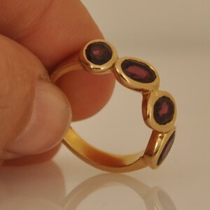 Puede incluir: Un anillo de oro con cinco piedras ovaladas de color rojo oscuro engastadas en la banda.