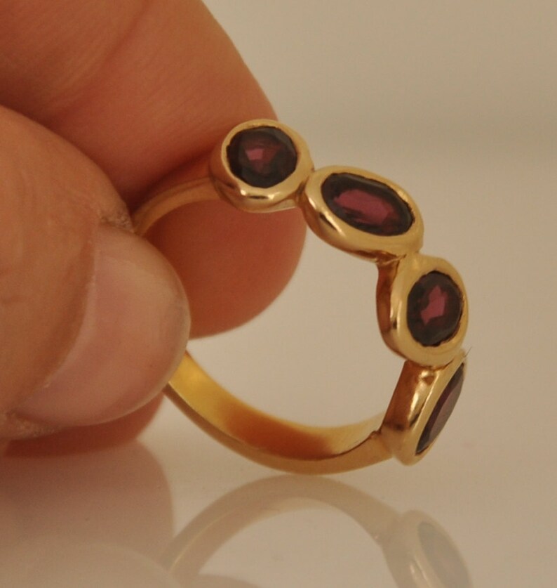 Puede incluir: Un anillo de oro con cinco piedras ovaladas de color rojo oscuro engastadas en la banda.
