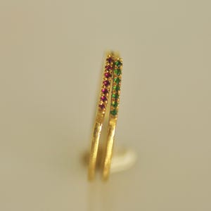 May include: Two gold rings with a row of small red and green gemstones.