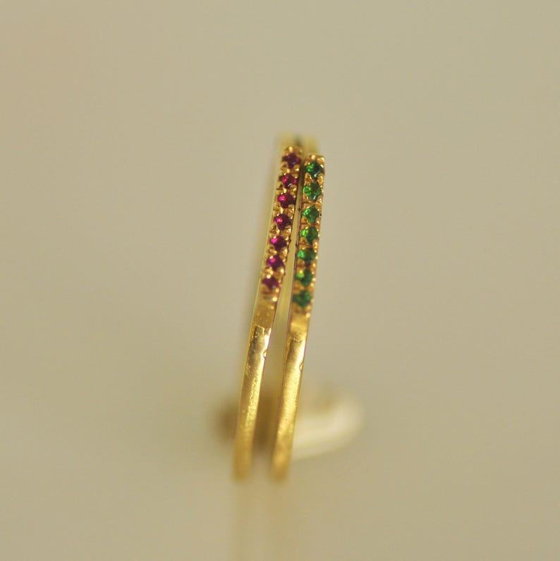 May include: Two gold rings with a row of small red and green gemstones.