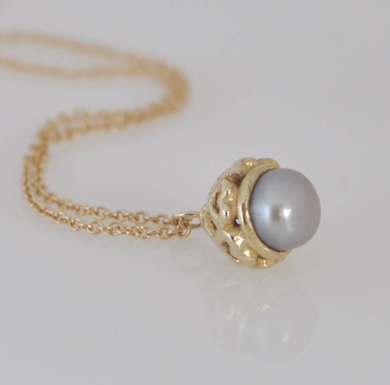 May include: A gold chain necklace with a delicate pendant featuring a gray pearl set in a gold filigree design.