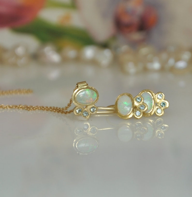 Op de afbeelding: Een gouden ketting met een hanger met een witte opaal omringd door kleine diamanten. De ketting wordt gecombineerd met een gouden oormanchet met drie witte opalen en kleine diamanten.