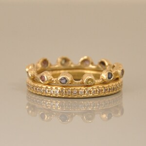 May include: Two gold rings with a row of small gemstones on the top ring and a row of small diamonds on the bottom ring.