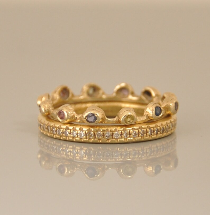 May include: Two gold rings with a row of small gemstones on the top ring and a row of small diamonds on the bottom ring.