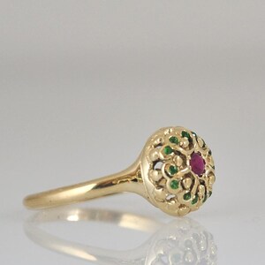 May include: A gold ring with a red gemstone surrounded by green gemstones in a filigree design.