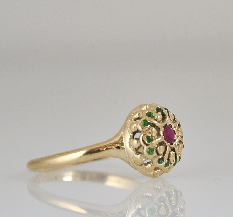 May include: A gold ring with a red gemstone surrounded by green gemstones in a filigree design.