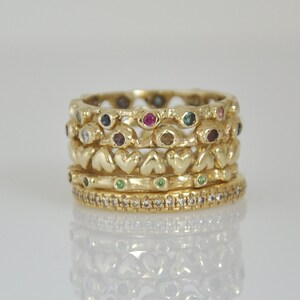 May include: A set of four gold rings with colorful gemstones and a heart-shaped design. The rings are stacked on top of each other.