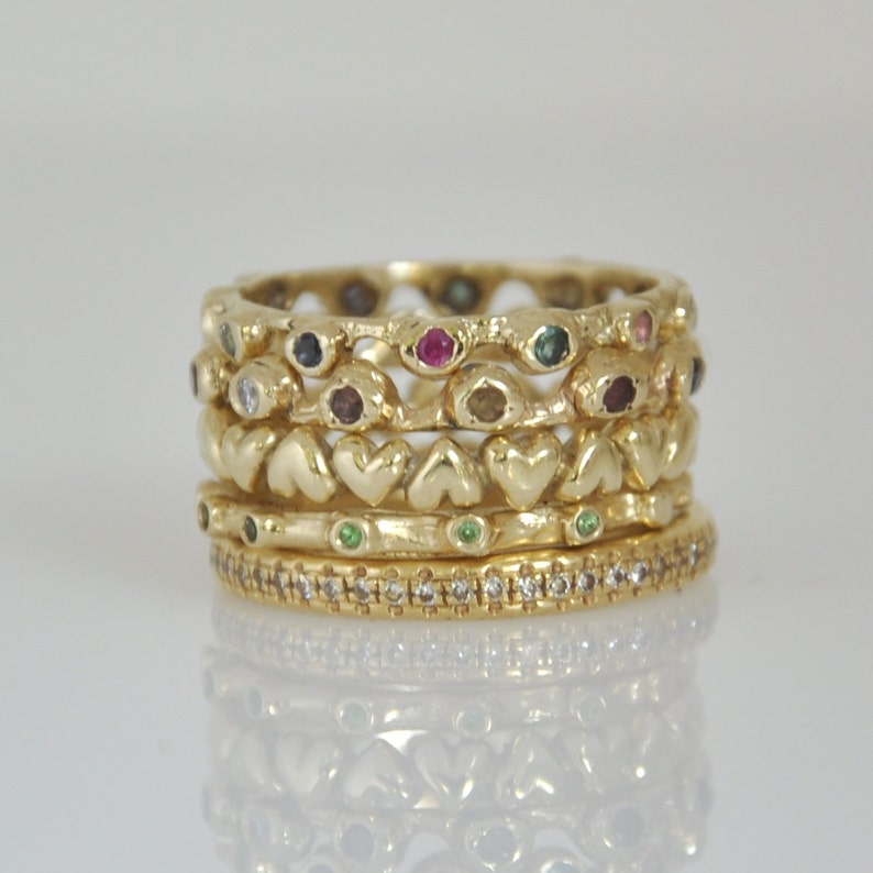 May include: A set of four gold rings with colorful gemstones and a heart-shaped design. The rings are stacked on top of each other.