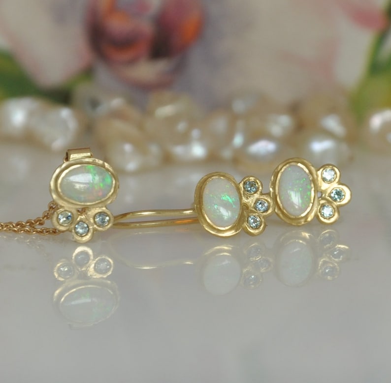 Op de afbeelding: Een paar gouden oorbellen met opaal- en diamantaccenten. De oorbellen zijn ontworpen met drie ovale opalen, elk omringd door kleine diamanten.
