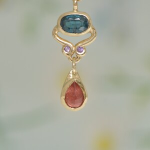 May include: A gold pendant necklace with a teardrop-shaped red gemstone, a blue gemstone, and two small purple gemstones.
