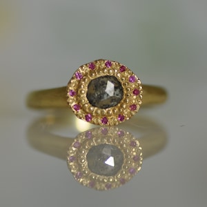May include: A gold ring featuring a grey diamond set within a halo of pink sapphires.