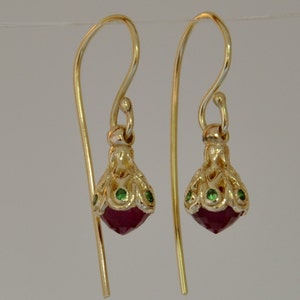 May include: Gold drop earrings featuring a red gemstone and green accents.