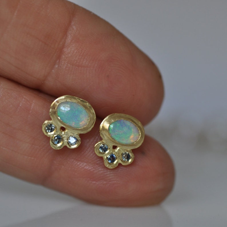 Op de afbeelding: Een paar gouden oorbellen met ovale opaal-edelstenen en kleine blauwe edelstenen.