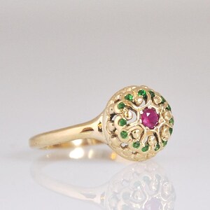 May include: A gold ring with a red ruby gemstone surrounded by green emeralds in a filigree design.