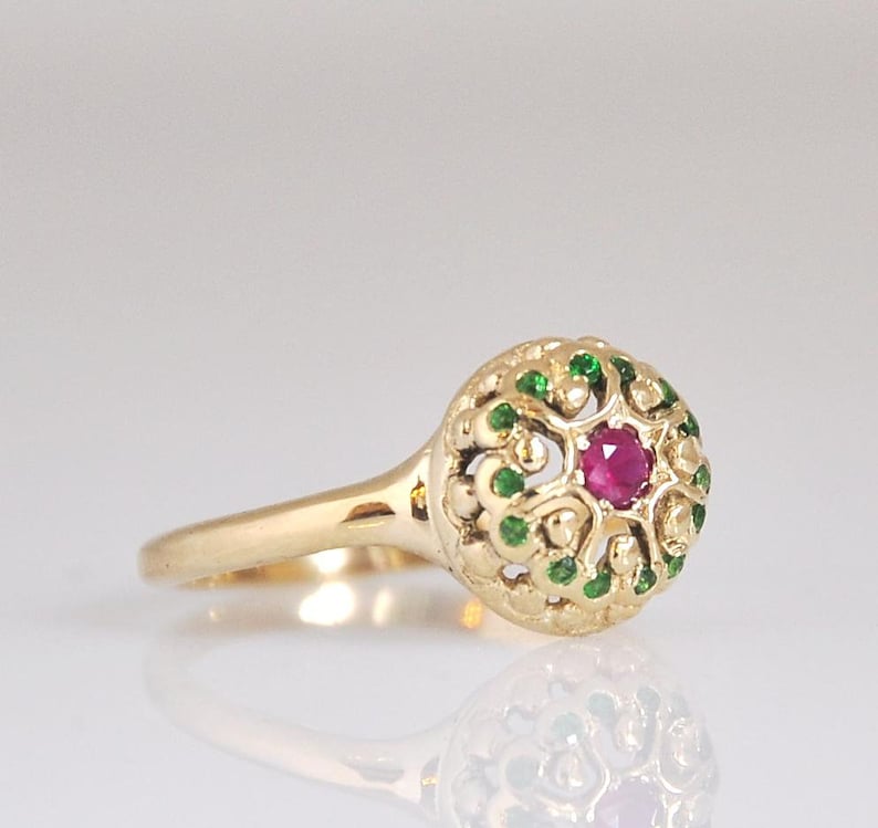 May include: A gold ring with a red ruby gemstone surrounded by green emeralds in a filigree design.