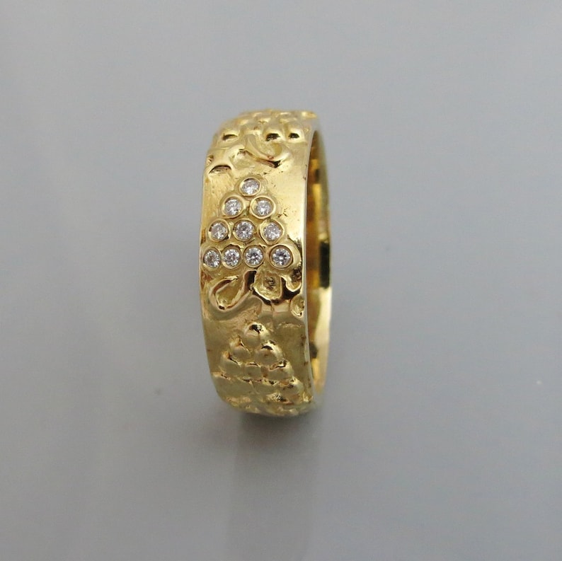 Puede incluir: Un anillo de banda de oro con una superficie texturizada y un grupo de peque&ntilde;os diamantes engastados en el centro.