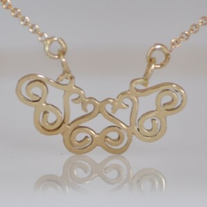 Puede incluir: Un collar de oro con un delicado y complejo colgante que presenta un dise&ntilde;o abstracto en espiral. El colgante tiene la forma de una mariposa con las alas extendidas.