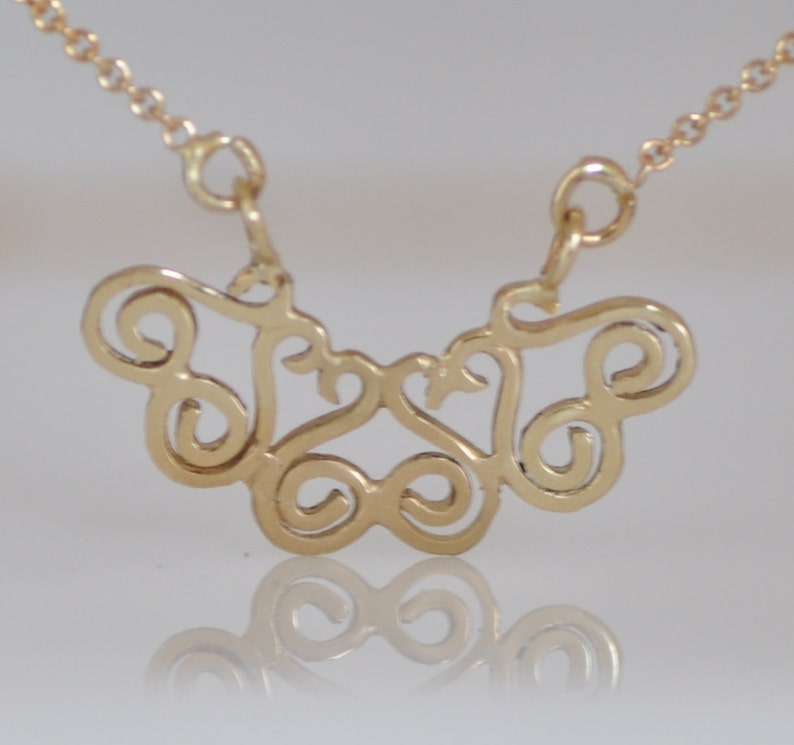 Puede incluir: Un collar de oro con un delicado y complejo colgante que presenta un dise&ntilde;o abstracto en espiral. El colgante tiene la forma de una mariposa con las alas extendidas.