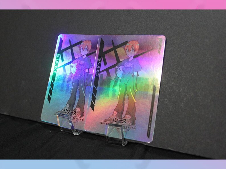 May include: Two holographic trading cards featuring an anime-style character with orange hair, wearing a purple shirt and green pants. The cards have Japanese text and the word "RESOURCE" in green.