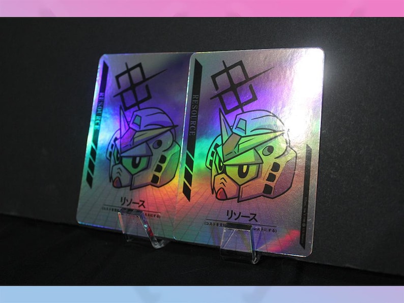 May include: Two holographic trading cards featuring a robot head design with green and yellow accents. The cards have Japanese text and the word "RESOURCE" printed on the side. They are displayed on a clear stand.