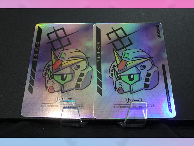 May include: Two holographic trading cards featuring a robot head design with green eyes, a yellow crest, and the word "RESOURCE" in a vertical column. Japanese text is also present. The cards are displayed on clear stands.