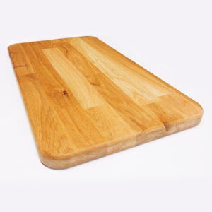 May include: A rectangular wooden chopping board with a light brown finish. The board has rounded edges and a smooth surface, showing the natural wood grain. Suitable for kitchen use.