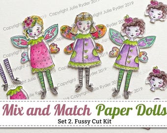 May include: A set of three illustrated paper dolls with fairy wings, featuring interchangeable parts including heads, dresses, and striped legs. The dolls have colorful watercolor-style outfits in pink, purple, and green, with floral accents.
