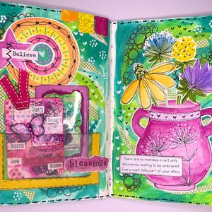 May include: A vibrant, open journal spread with mixed media art. The left page features a star with "Believe" and a collage with "Create, Balance, Breathe, Grow, Wisdom, Blessings". The right page has a pink vase with flowers and text: "There are no mistakes in art..."