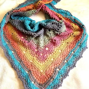 May include: A colorful, handmade crochet shawl. The shawl features a vibrant spectrum of colors, including blue, teal, pink, orange, yellow, and gray. The triangular shawl has a detailed, openwork design with a scalloped edge, perfect for adding a touch of handmade charm to any outfit.