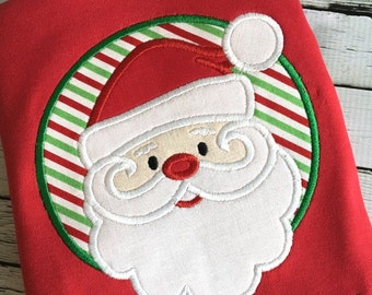 Puede incluir: Diseño bordado de la cara de Papá Noel con barba blanca y gorro rojo, rodeado de un círculo de rayas verdes y rojas.