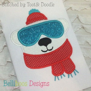 May include: Embroidered design of a polar bear wearing a red and white hat, blue goggles, and a red and white scarf with white polka dots. The design is stitched on a white fabric with the text "Stitched by Toot & Doodle" and "Bellikoo's Designs" at the top and bottom.