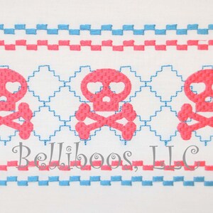 Puede incluir: Tres diseños de calaveras y huesos cruzados de color rosa con corazones por ojos, bordados sobre un fondo de tela blanca con bordes a cuadros azules y rosas. El texto "Belliboos, LLC" está bordado debajo de las calaveras.
