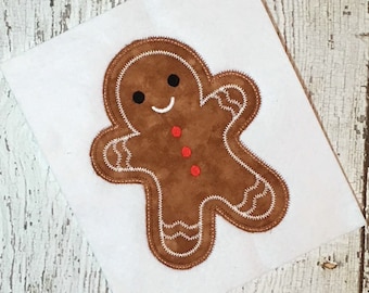 May include: A brown gingerbread man applique with white stitching and red buttons. The gingerbread man has a smiling face with black eyes.
