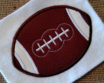 May include: A brown and white embroidered football design on a white fabric background.